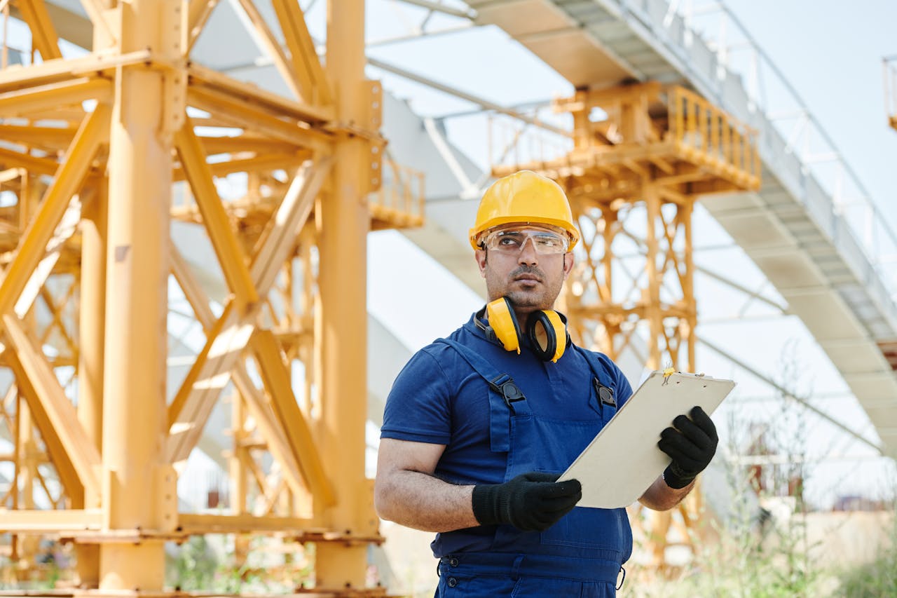 Worker in safety gear inspecting construction site with clipboard.
